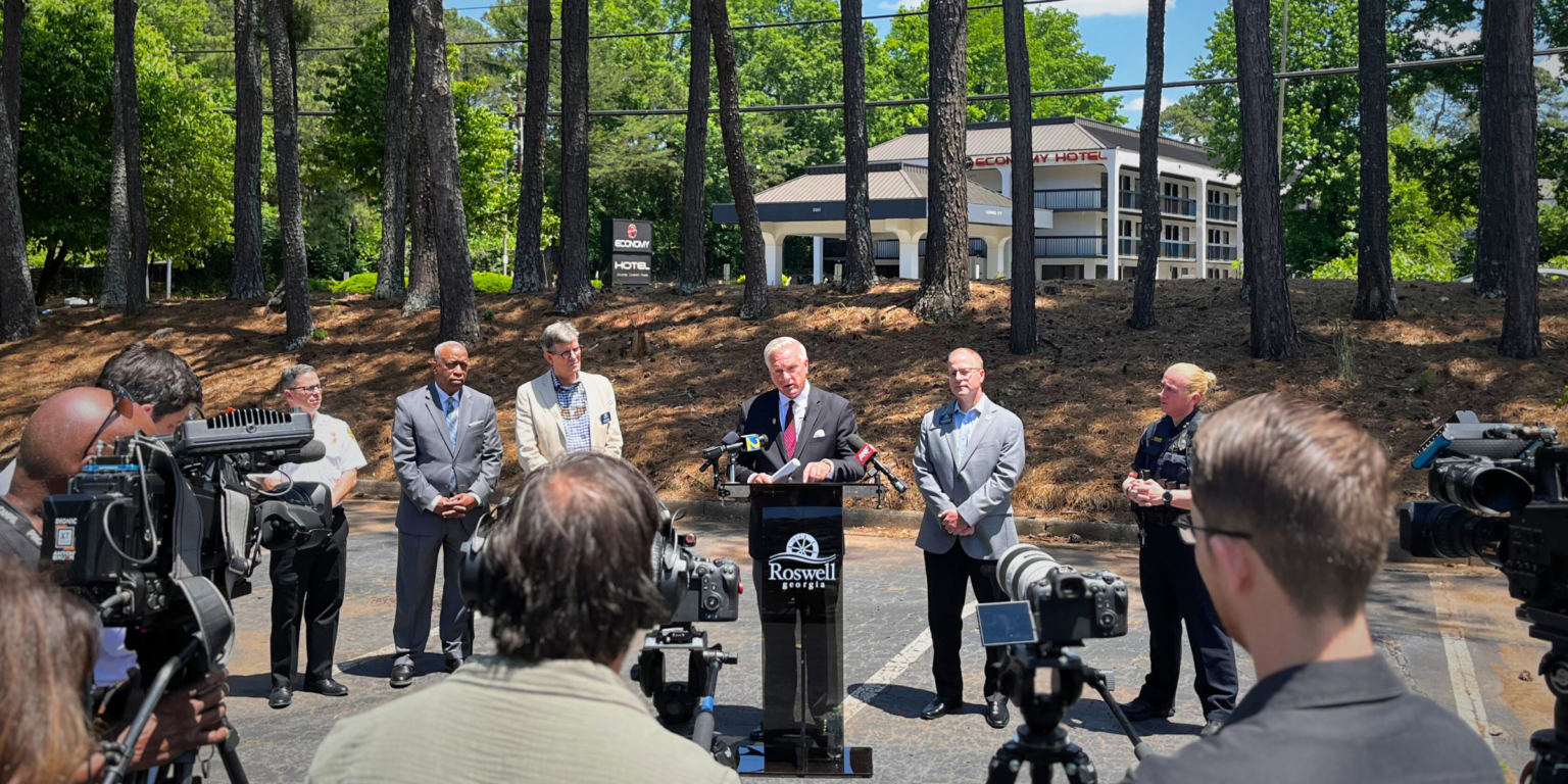 This is a photo of Mayor Kurt Wilson and City leaders at a press briefing in front of the Economy Hotel.